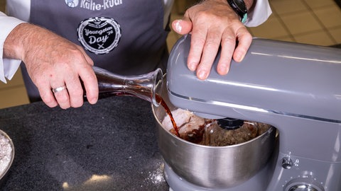 Ein Konditor gibt aus einer Glaskaraffe Rotwein in eine Teigmischung.