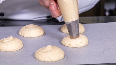 Der Teig der Amerikaner wird auf ein Backpapier gespritzt.