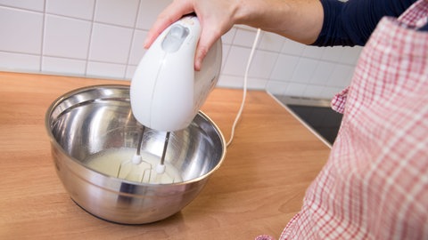 Eine Frau rührt Zuckerguss mit einem Handmixer an