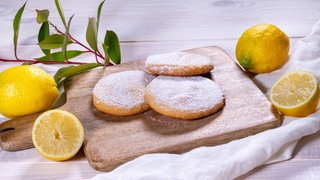 Die frischen Cookies (Zitronenkekse) liegen nach dem Backen, wie im Rezept beschrieben, auf einem Holzbrett angerichtet.