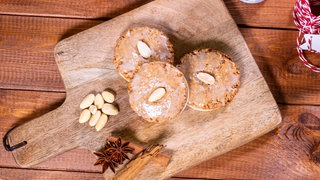Nach dem Backen liegen die Lebkuchen auf einem Holzbrett. Die Elisenlebkuchen sind wie im Rezept beschrieben mit Zuckerguss glasiert und Mandeln dekoriert. 