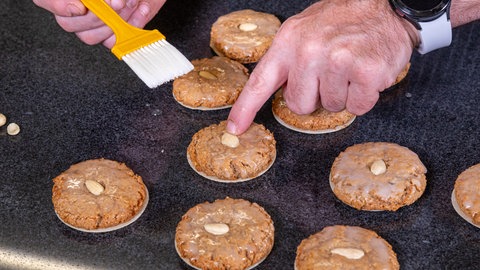 Die Lebkuchen liegen kurz nach dem Backen auf der Arbeitsplatte. Wie im Rezept beschrieben werden sie nun ganz einfach mit Zuckerguss glasiert und mit einer Mandel dekoriert.