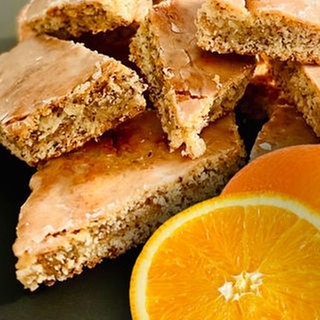 Plätzchen backen für Advent und Weihnachten: Mehrere Mohn-Orangen-Plätzchen liegen auf einem Haufen, im Vordergrund eine ganze Orange und eine Orangenscheibe