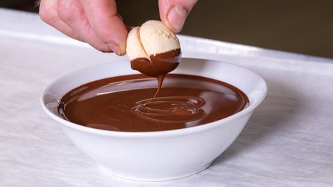 Vanillebrötchen backen: Ein Plätzchen wird in flüssige Schokolade getaucht.