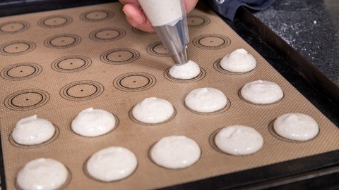 Mit der Lochtülle wird der Teig auf das Backpapier dressiert.