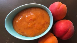eine Schale mit Aprikosenmarmelade und drei frischen Aprikosen