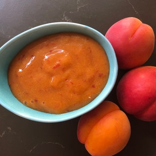 eine Schale mit Aprikosenmarmelade und drei frischen Aprikosen