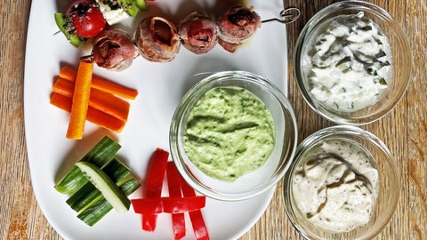 Rezept für Frischkäse-Dips selber machen: Auf einem weißen Teller liegen zwei Gemüsespieße, eine Schüssel mit einem Dip und mehrere Gemüsesticks, kunstvoll arrangiert. Daneben stehen zwei kleine Schüsseln mit jeweils einem Dip gefüllt.