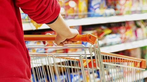Person schiebt ihren Einkaufswagen durch die Gänge eines Supermarktes.