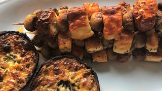 Gefüllte Portobellos und PIlzspieße schön knusprig gegrillt auf einer weißen Porzellanplatte. Pilze sind kalorienarm und machen lange satt. Vielfältig variiert sind sie ideal auf dem Grill oder als Antipasti. Gut gewürzt schmecken sie hervorragend als Ersatz für Fleisch.