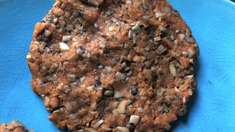 Ein Patty für einen Burger aus gehackten Pilzen, hier Champignons, liegt auf einem Teller.