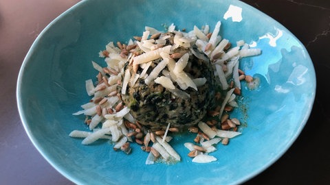 Spinatknödel mit Parmesan und Pinienkernen auf einem blauen Teller angerichtet. 