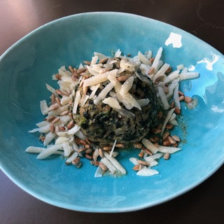 Spinatknödel mit Parmesan und Pinienkernen auf einem blauen Teller angerichtet. 