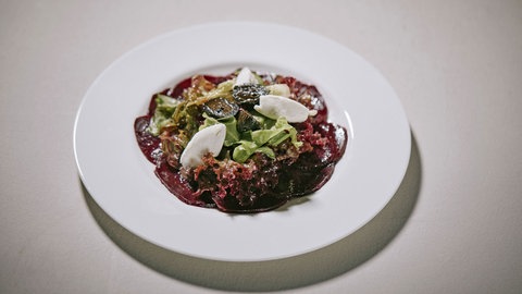 Rote Bete Carpaccio mit Ziegenfrischkäse und schwarzen Nüssen auf einem Teller