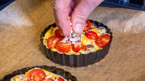 Die vegetarische Quiche mit Tomaten und Mandelstiften garnieren.
