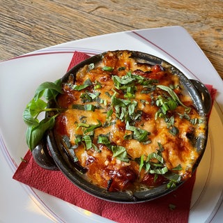 braune Auflaufform mit Auberginenauflauf mit Basilikumblättern als Deko