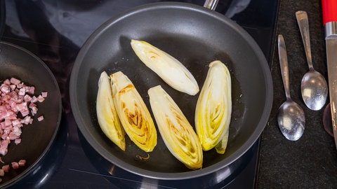 Chicoree-Hälften werden in einer Pfanne bräunlich gebraten.