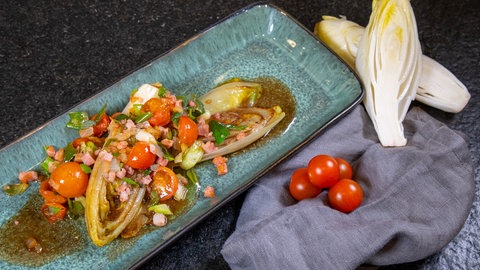 Chicoree in der Pfanne gebraten mit einem Topping aus Speck, Zwiebeln und Kirschtomaten.