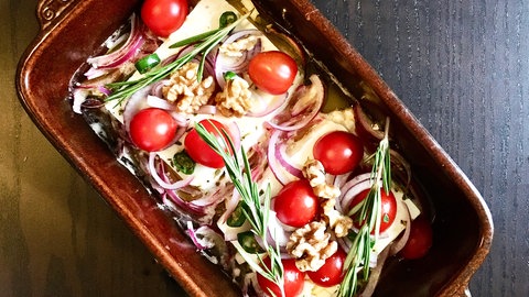 braune, eckige Form mit Feta, der mit kleinen Tomaten und Zwiebeln und Rosmarin bedeckt ist.