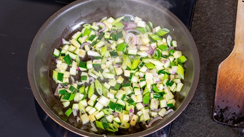 Die vegetarische Füllung für den Hokkaido-Kürbis in einer Pfanne. Es befinden sich darin Zucchini, Schalotten und Lauch.