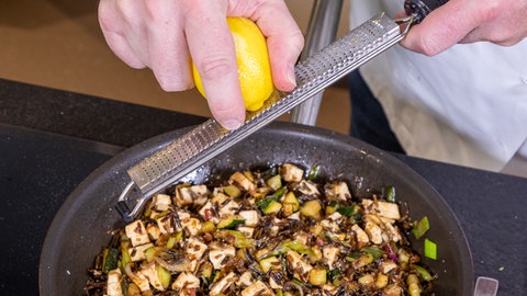 Eine Zitronenschale wird abgerieben und der vegetarischen Füllung für den Hokkaido-Kürbis zugegeben.