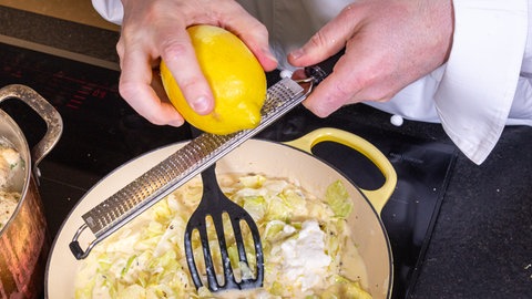 In die Pfanne mit dem köchelnden Spitzkohl bzw. Filderkraut in Sahnesoße wird die Schale einer Zitrone gerieben.