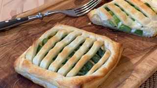 Grüner Spargel im Blätterteig liegt auf einem Holzbrett. Es ist ein SWR1 Pfännle Rezept von SWR1 Koch Eberhard Braun.