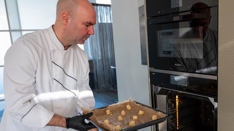 Eberhard Braun schiebt ein Blech mit Käsechips in den Backofen