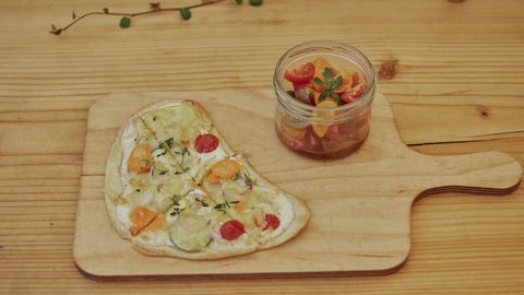 Flammkuchen mit Gemüse und buntem Tomatensalat auf einem Brett