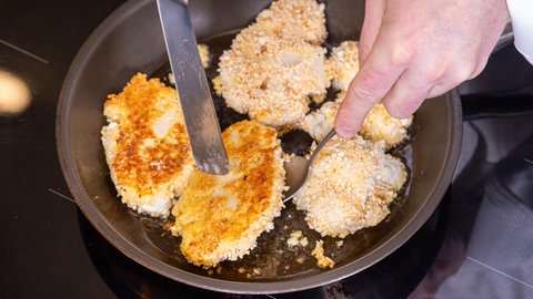 Schnitzel aus Blumenkohl werden in einer Panade nach Rezept in einer Pfanne knusprig gebraten.