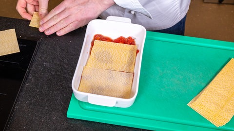 Die Tomatensoße und Lasagneblätter werden in eine Auflaufform geschichtet.