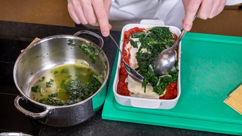 Der Spinat wird auf die Sahnesoße geschichtet. Darunter befindet sich Tomatensoße.