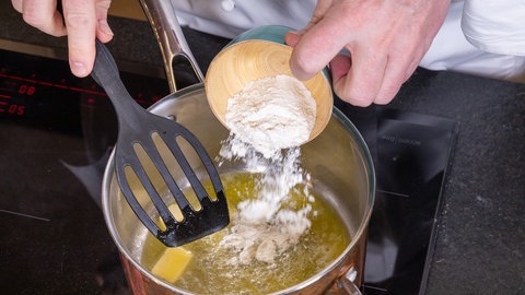 Das Mehl wird in einen Topf mit geschmolzener Butter gegeben, um eine Mehlschwitze herzustellen.