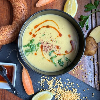 Linsensuppe in einer schwarzen Schale auf einem Holztisch. Drumherum liegen verschiedene Zutaten.