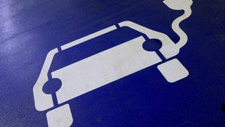 Parkplatz für E-Auto. Auf dem Boden befindet sich ein aufgesprühtes Fahrzeug mit einem Elektrokabel auf blauem Untergrund. E-Autos sind laut einer neuen Studie so langlebig wie Verbrenner.