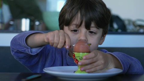 Junge isst Ei. Eier erfreuen sich bei vielen Menschen, jung und alt, großer Beliebtheit. Aber die Vorstellungen darüber, wie das perfekte gekochte Ei beschaffen sein sollte, gehen oft weit auseinander.