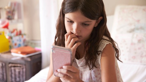 Mädchen sieht besorgt auf ihr Smartphone. Smartphones Kinder Gefahren