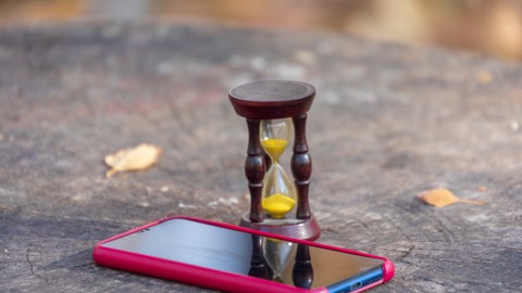 Symbolbild Bildschirmzeit: Sanduhr liegt neben Smartphone. Smartphones Kinder Gefahren
