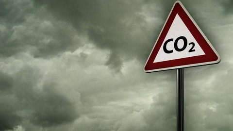 CO2-Warnschild vor grauen Wolken: Der Treibhauseffekt beginnt teilweise schon unmittelbar über der Erdoberfläche, indem einfach Gase wie CO2, Methan und Wasserdampf die Wärmestrahlung von der Erde absorbieren und einen Teil diese Wärme wieder zurück zur Erdoberfläche abstrahlen. Um diesen Effekt zu entfalten, müsste das CO2 gar nicht in die Höhe aufsteigen. Trotzdem gelangt es in die obere Atmosphäre und dort entfaltet es eine zusätzliche Wirkung.