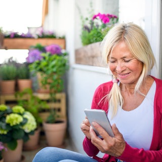 Eine Frau sitzt auf dem Balkon und tippt auf ihr Smartphone