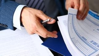 Männlicher Arm in einem Anzug durchsucht Versicherungsunterlagen