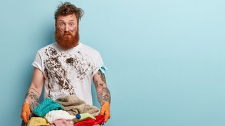 Der Fleck muss weg: Ein Mann mit schmutzigem Shirt trägt einen Wäschekorb voller Schmutzwäsche