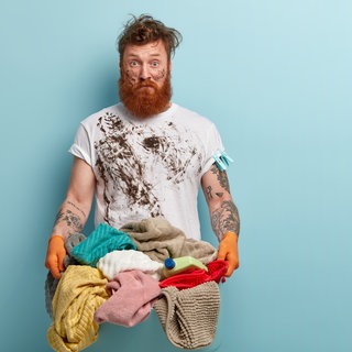 Der Fleck muss weg: Ein Mann mit schmutzigem Shirt trägt einen Wäschekorb voller Schmutzwäsche
