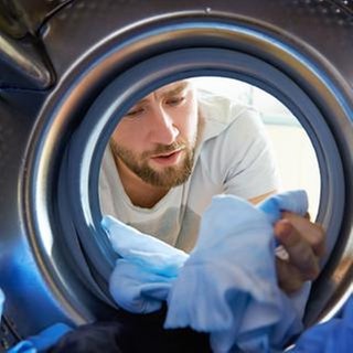 Mann begutachtet kritisch die Wäsche, die er aus seiner Waschtrommel zieht.