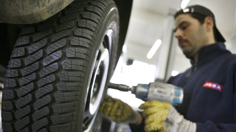 Ein Monteur zieht in einer Werkstatt Winterreifen beim Wechsel des Autoreifens auf.