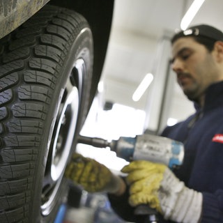 Ein Monteur zieht in einer Werkstatt Winterreifen beim Wechsel des Autoreifens auf.
