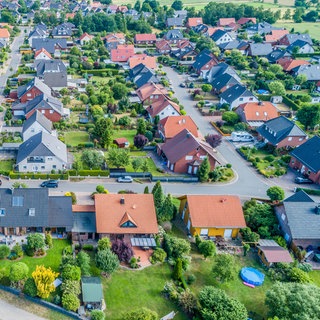 Häuser in direkter Nachbarschaft zueinander. Bäume und Hecken säumen die Grundstücksgrenzen.