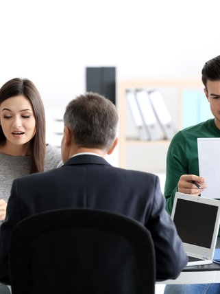 Eine junge Frau und ein junger Mann sitzen mit Dokumenten in der Hand beim Notar. Welche Rechte haben Kinder und Stiefkinder in Bezug auf den Pflichtteil beim Erbe?