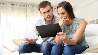 Mann und Frau grübeln über ihrem Tablet. Recht haben und bekommen sind oft verschiedene Dinge. Die Rechtsschutzversicherung soll vor Gericht helfen. Was kann sie vorschreiben? Und was tun, wenn der Versicherer kündigt?