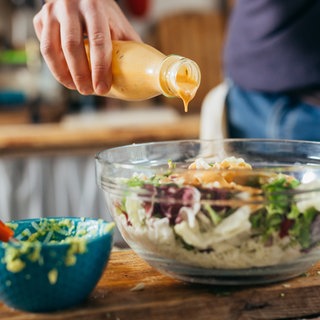 Eine Person schüttet Dressing aus einer Flasche auf einen Salat.